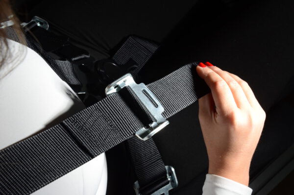 Sim racing harness – adjusting a shoulder strap Hand adjusting a harness shoulder strap using its metal adjuster