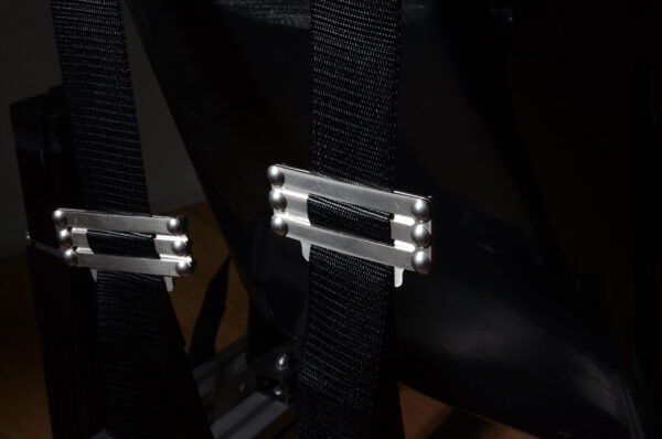 Sim racing harness – rear shoulder strap adjusters Two harness shoulder straps and metal adjusters behind a racing seat